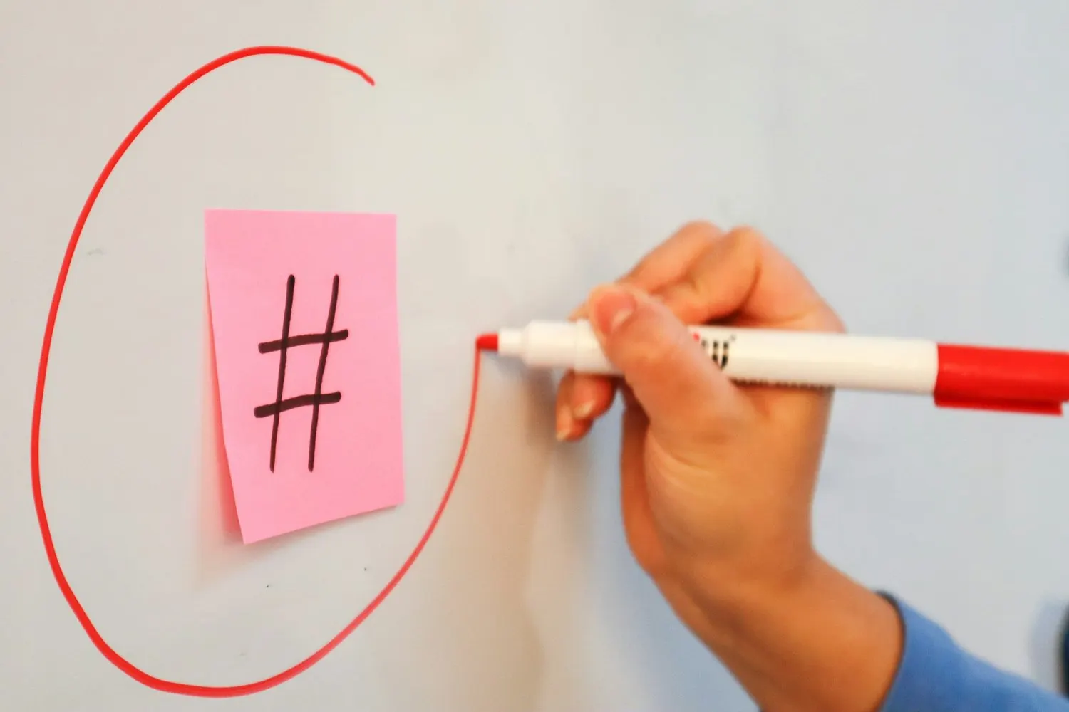 Hand drawing a circle around a hashtag symbol on a sticky note.