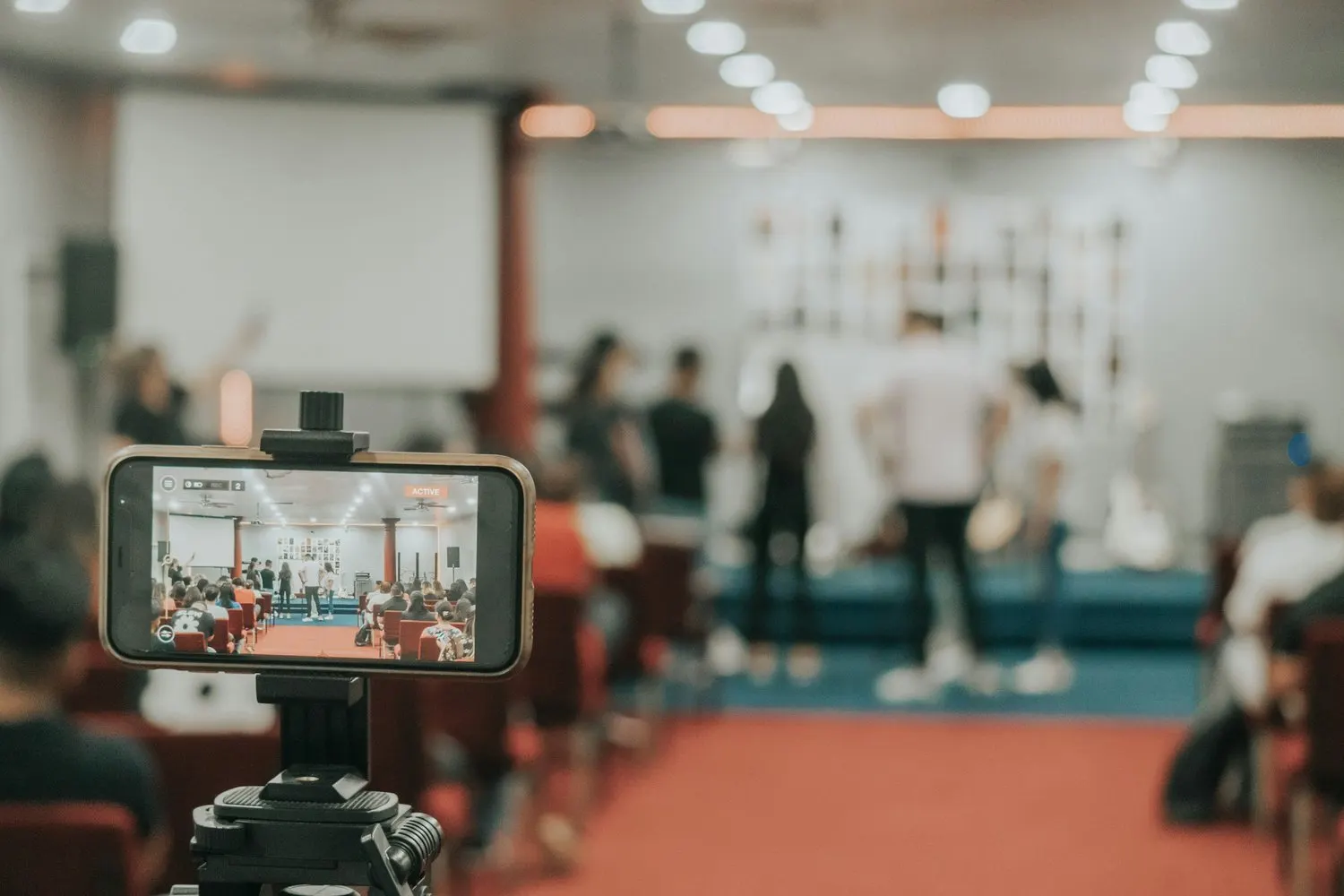Smartphone on a tripod recording a live event in an auditorium.