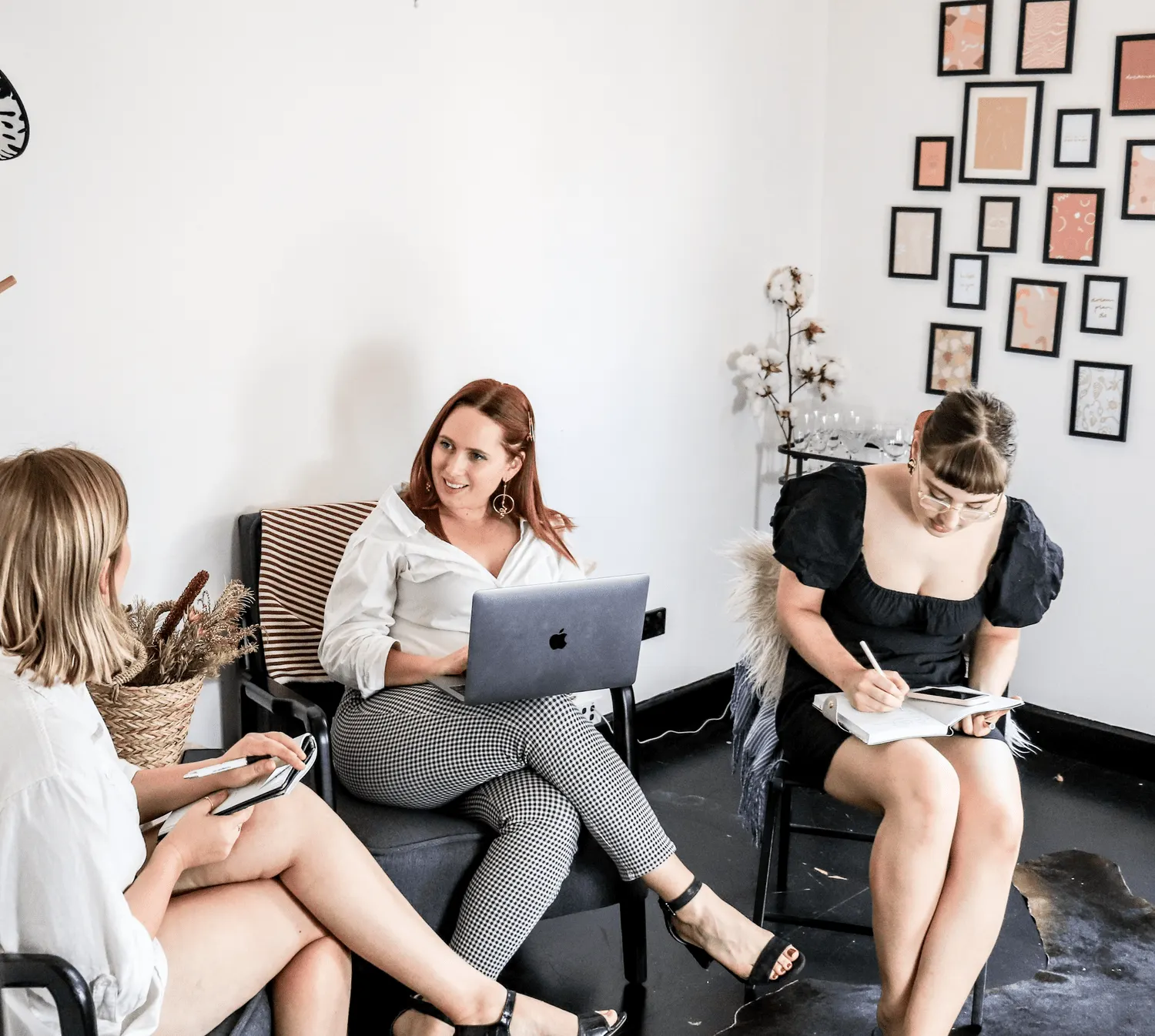 Three women collaborating in a modern meeting space with laptops and notebooks.