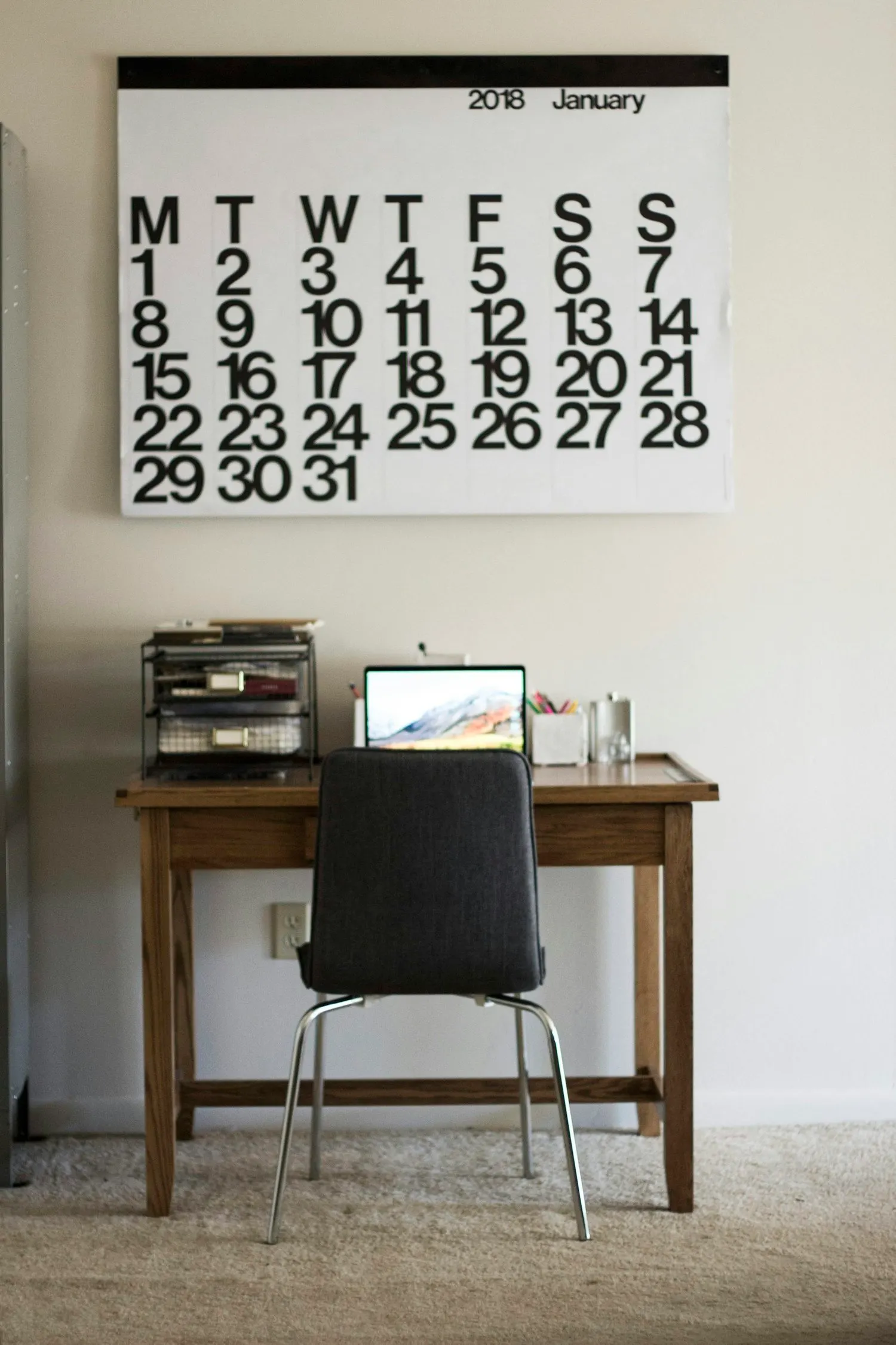 Minimal home office with a large wall calendar above a desk.