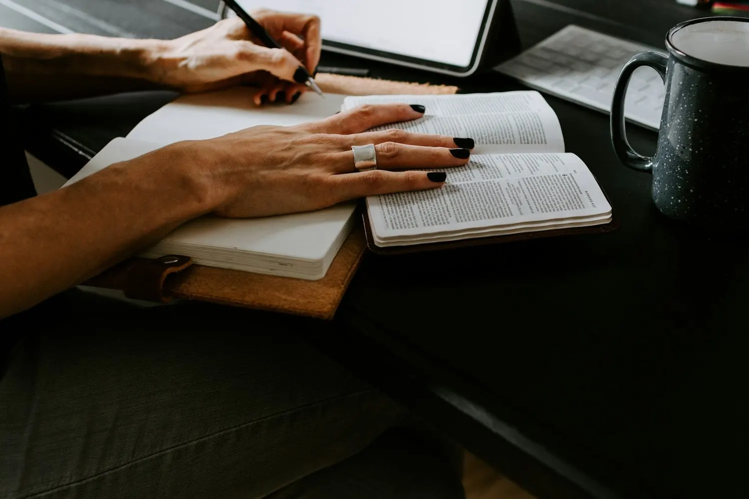 Person studying scripture and taking notes at a desk with coffee.