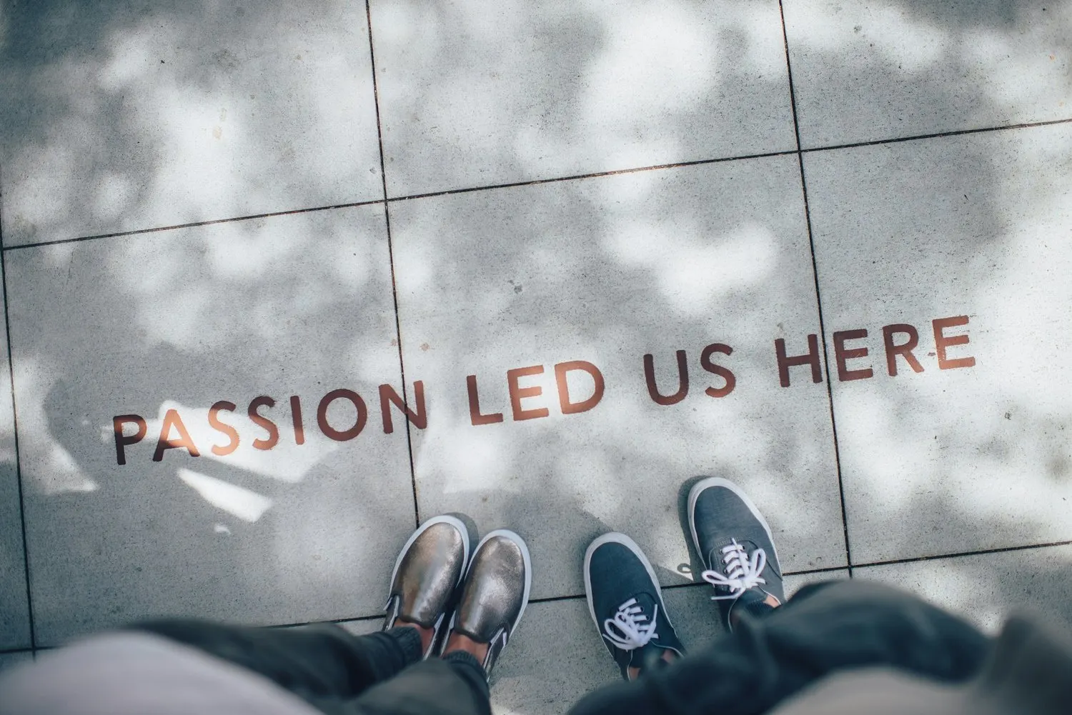 Two people standing beside the phrase ‘Passion Led Us Here’ on a sidewalk.