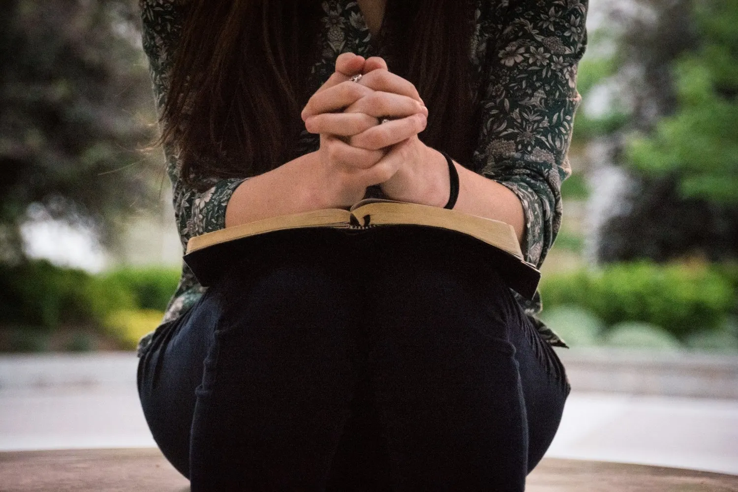 Person praying over an open Bible outdoors.
